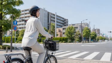 電動アシスト自転車に乗る大人がヘルメットを着用して交差点で停止している様子
