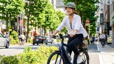 電動アシスト自転車に笑顔で乗るヘルメットをかぶった日本人女性