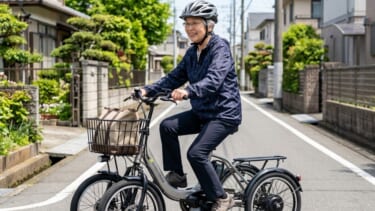 住宅街をヘルメットを着用して笑顔で走行するシニアの四輪電動アシスト自転車